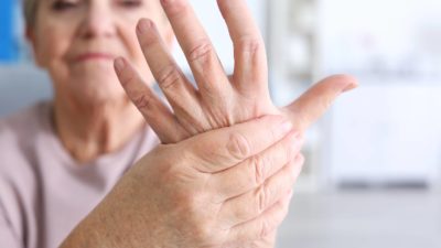 older adult gripping her sore hand because of arthritis